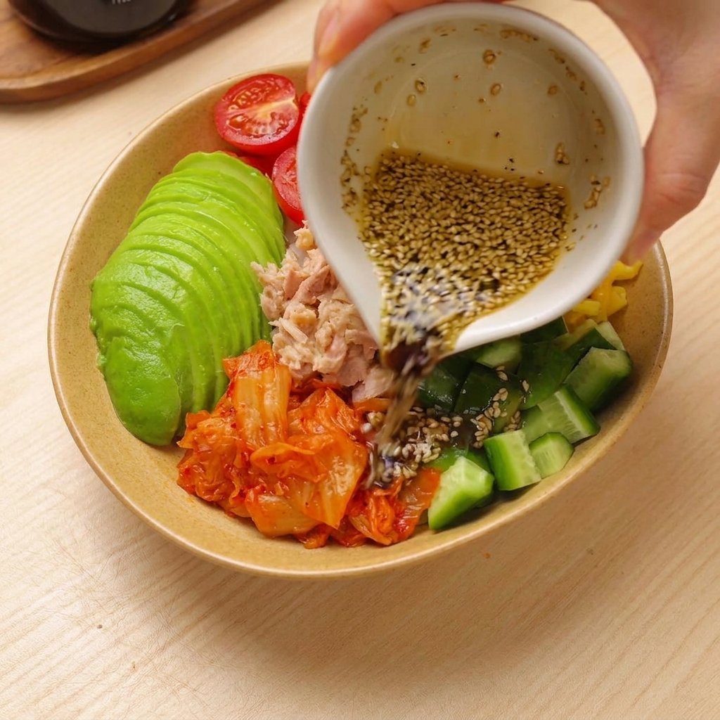 De la vinaigrette versée sur un bol de riz coloré assemblé au thon et à lavocat.