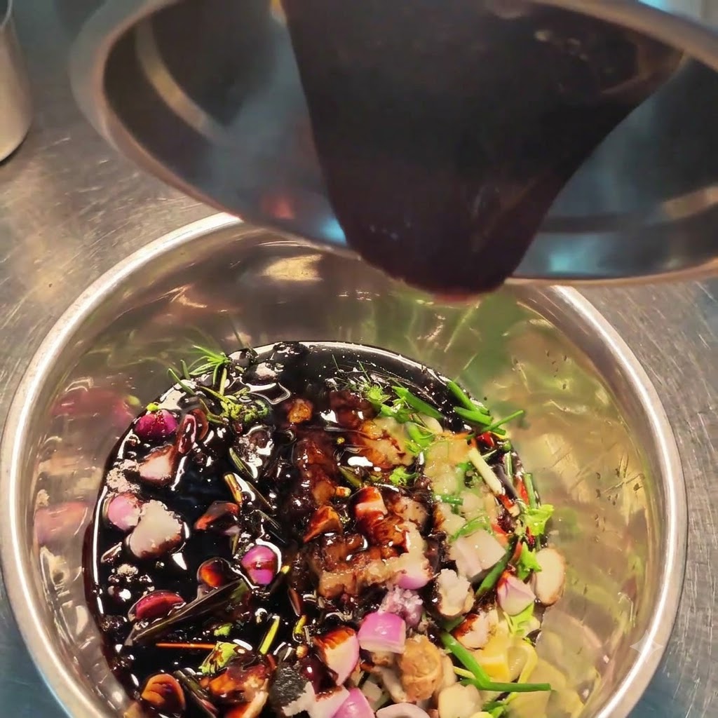 Sauce sombre versée dun récipient en acier dans un bol rempli de diverses herbes, épices et aromates hachés.