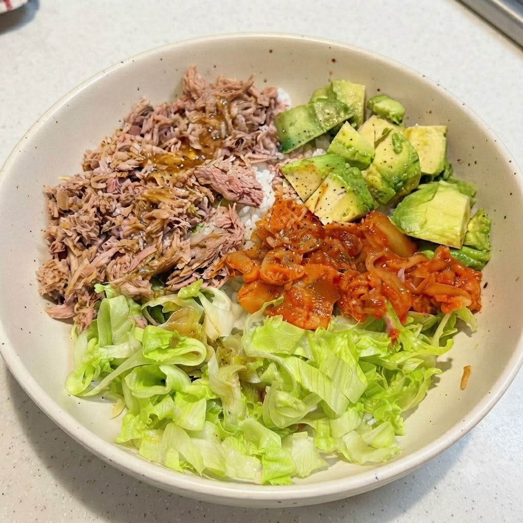 Un bol de riz au thon et à lavocat assemblé avec de la vinaigrette arrosée sur les ingrédients du dessus.
