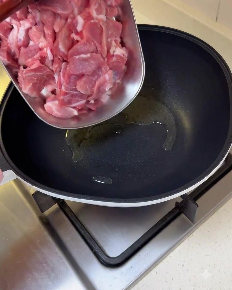Des morceaux de porc cru tranchés transférés dun plateau vers une poêle huilée.