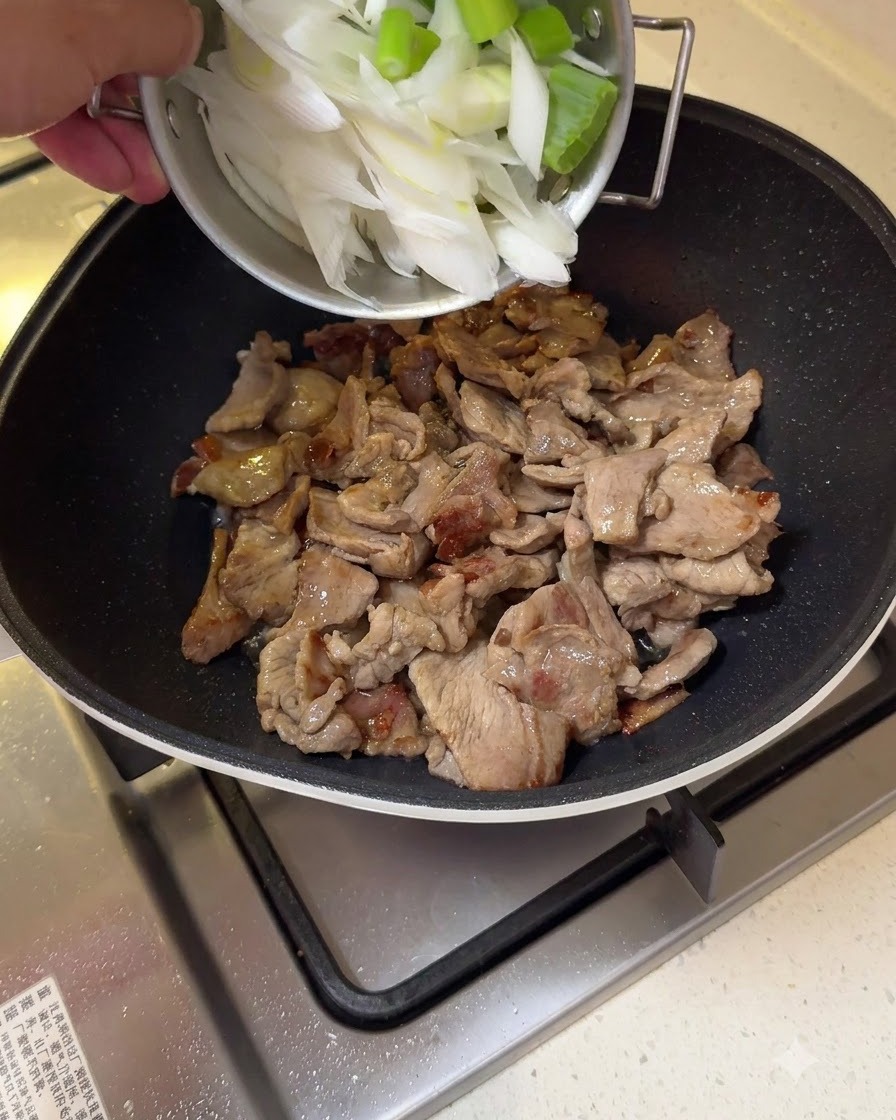 De gros morceaux doignon vert hachés ajoutés au porc sauté dans une poêle.