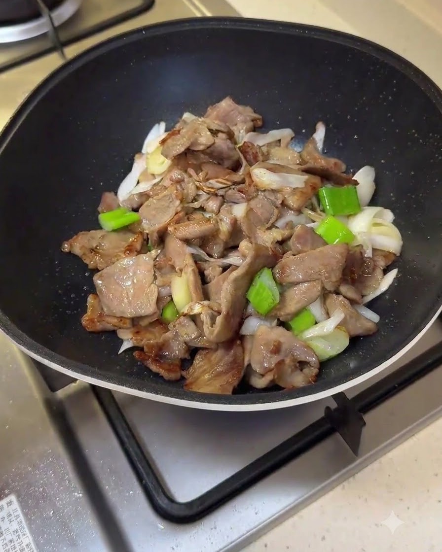 Le mélange de sauce rouge versé dans la poêle sur le porc et les oignons verts.
