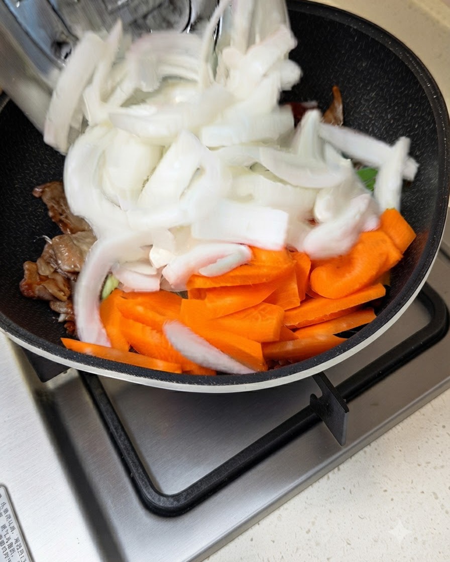 Des oignons blancs et des carottes tranchés ajoutés dans une poêle avec de la viande en train de sauter et de la sauce.