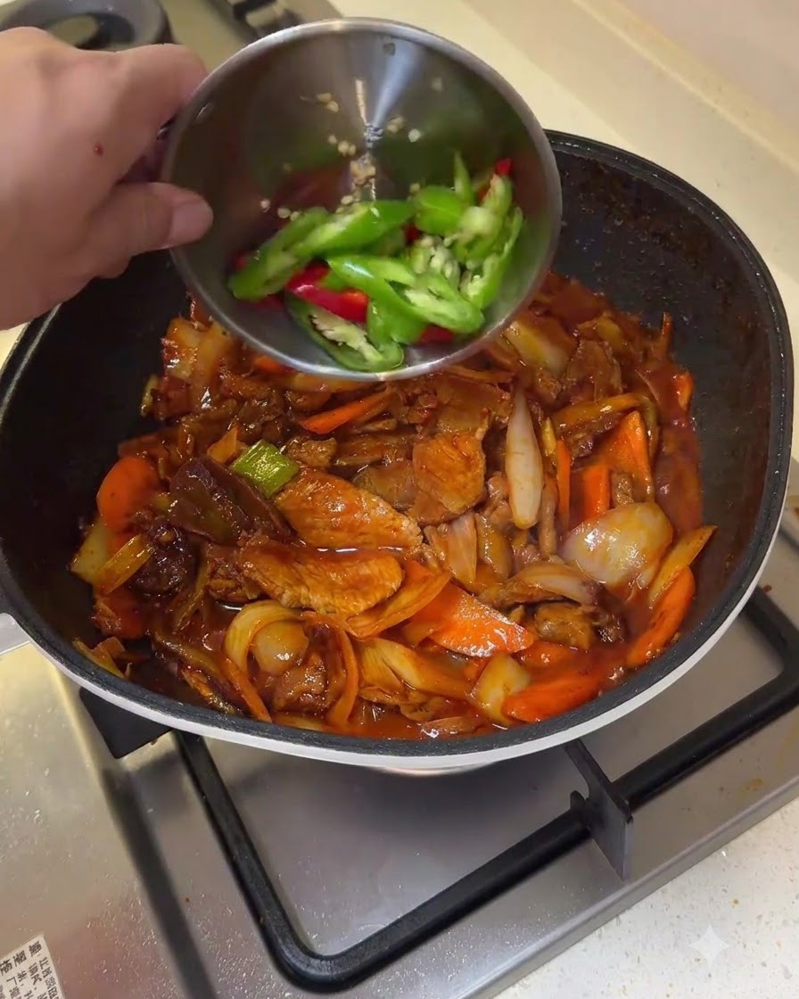Des tranches de piments verts et rouges versées dun petit bol dans une poêle de porc sauté et de légumes.