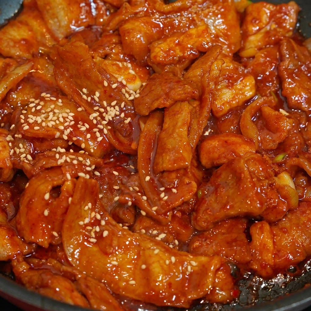 Un plan rapproché de graines de sésame blanc saupoudrées sur des tranches de porc épicé rouge et en sauce dans une poêle.