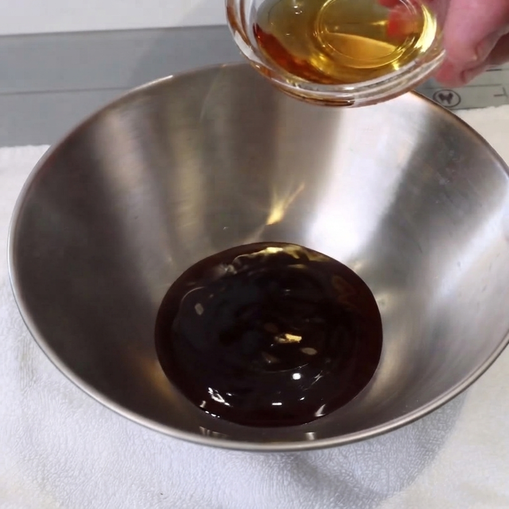 Un petit bol en métal avec des ingrédients liquides mélangés avec une cuillère sur une serviette blanche.