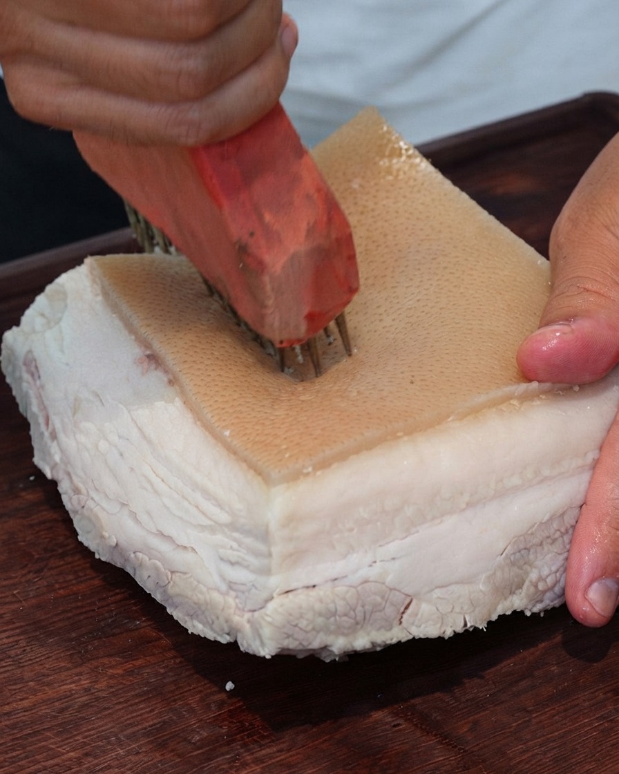 Gros plan dun outil à piquer la viande perçant des trous à plusieurs reprises dans la surface de la peau de porc.