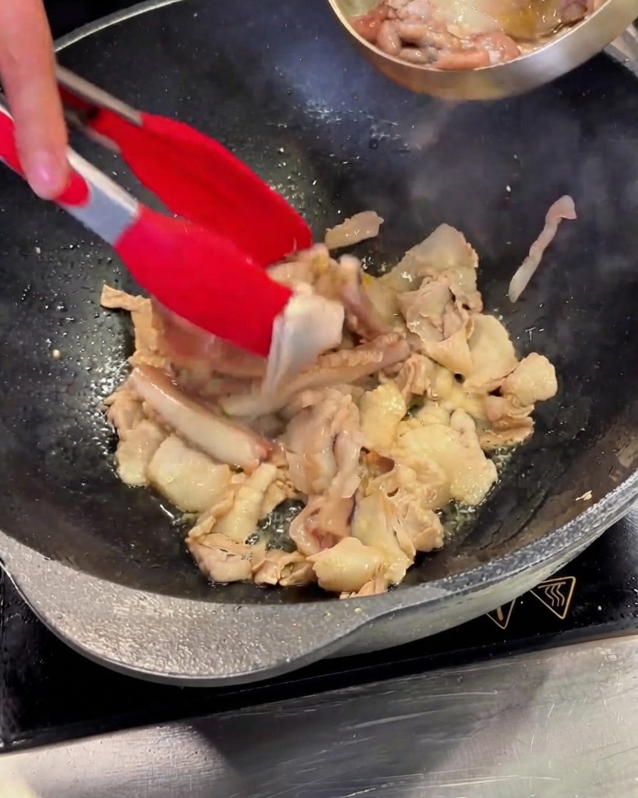 Morceaux de calamar nettoyés versés depuis un bol en inox dans le wok contenant le porc.