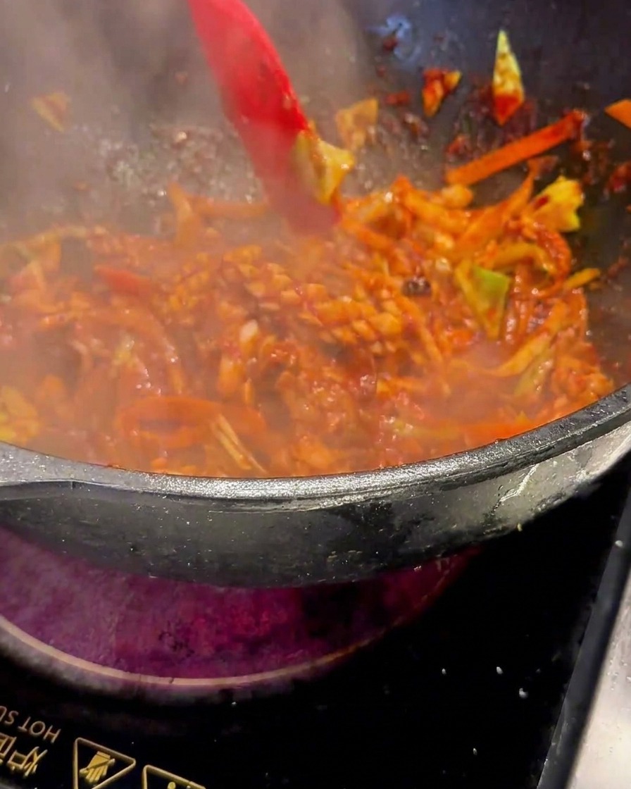 Spatule rouge remuant la préparation crépitante dans le wok à feu vif.
