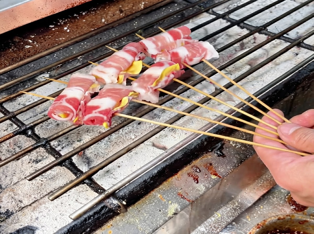 Plusieurs rouleaux de viande sur des brochettes disposés sur une grille de barbecue à charbon chaud pour une cuisson lente.
