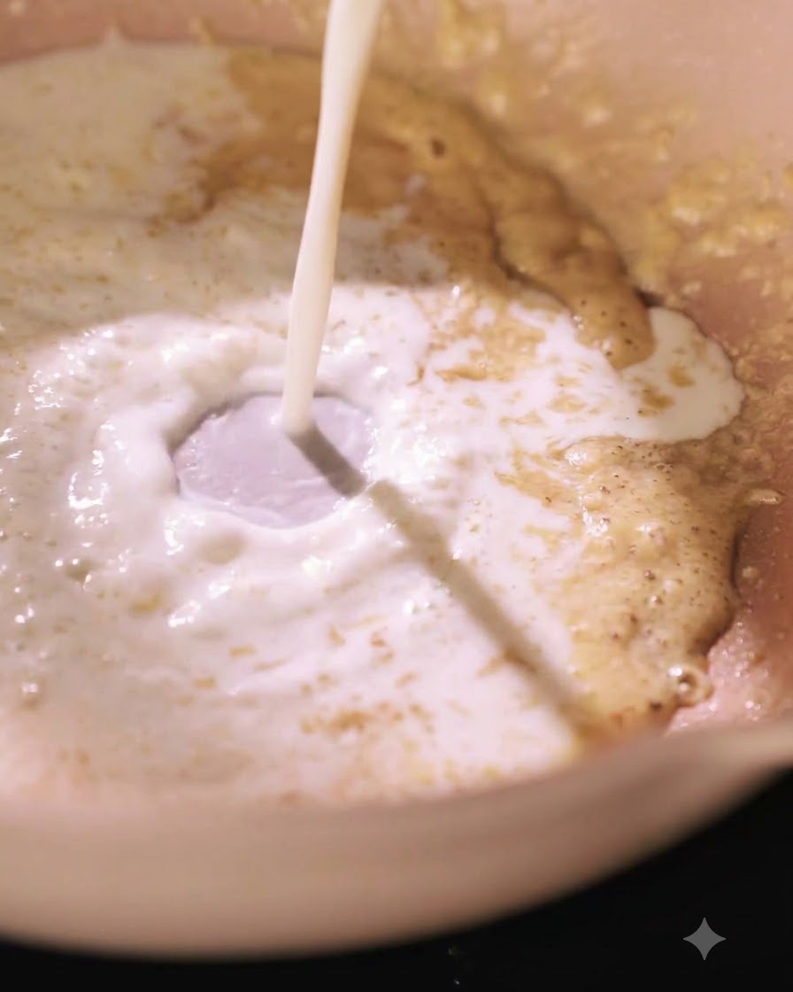 Du lait versé dans une poêle contenant un mélange de roux, créant un tourbillon.