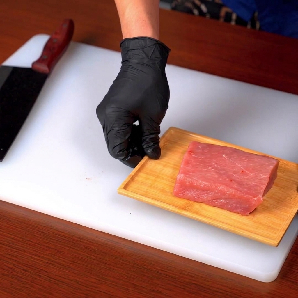 Un morceau de filet de porc cru en train dêtre tranché sur une planche en bois posée sur un plan de travail blanc.