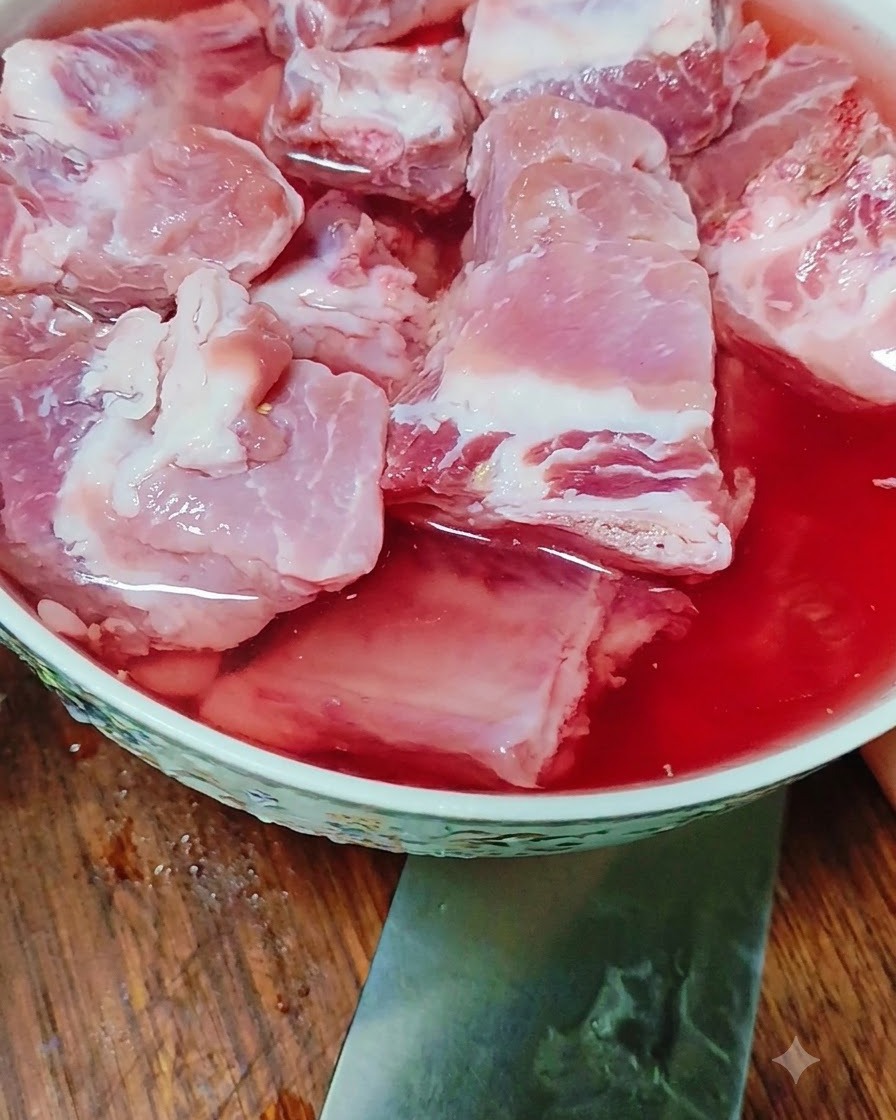 Côtes de porc crues trempant dans un bol deau teintée de rouge.