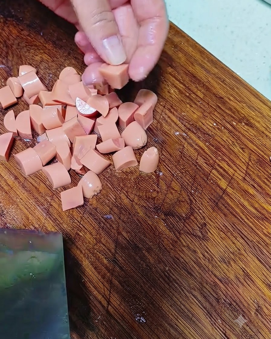 Mains coupant une saucisse en petits morceaux sur une planche à découper en bois.