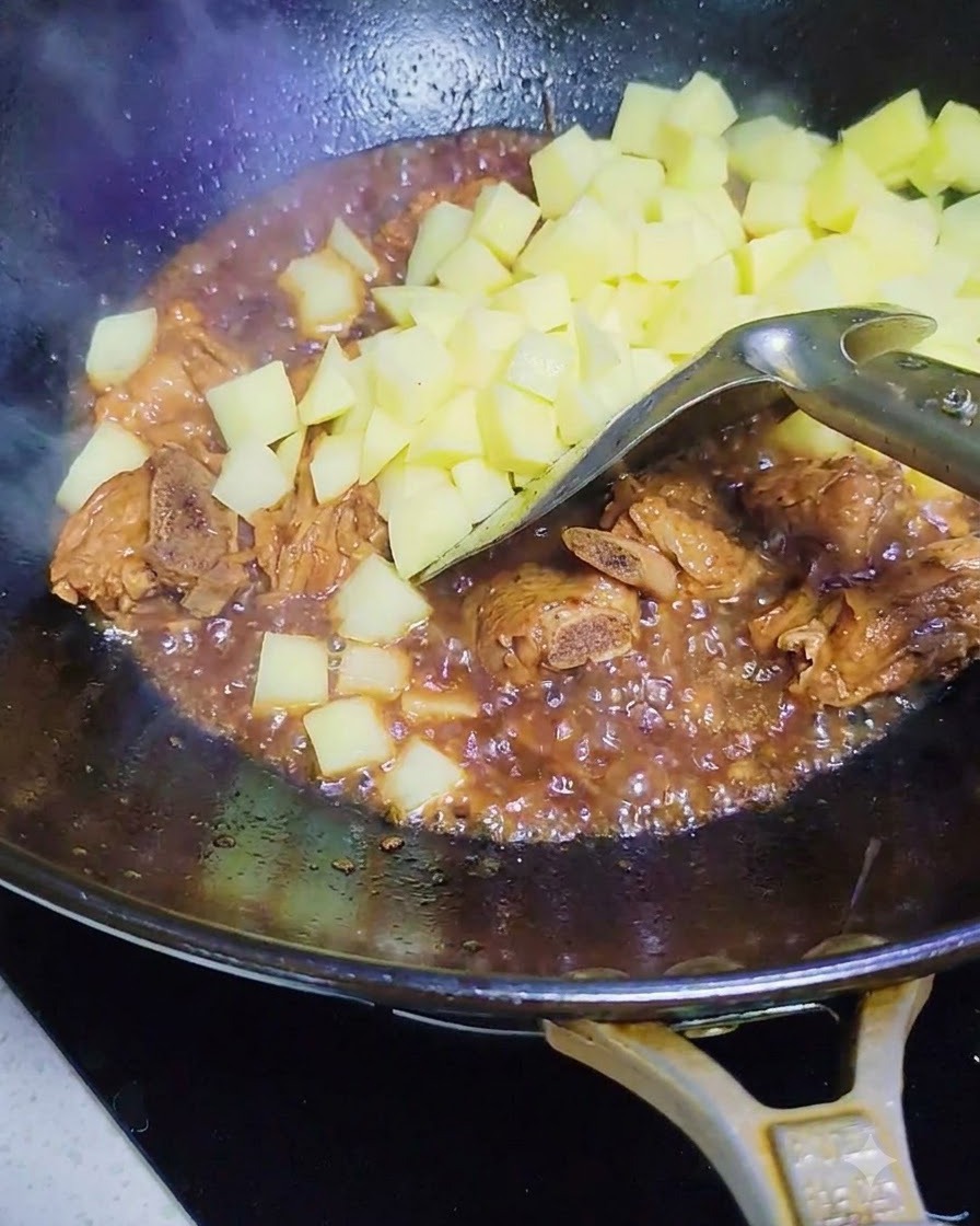 Dés de pommes de terre crues ajoutés dans le wok avec les côtes de porc et la sauce.