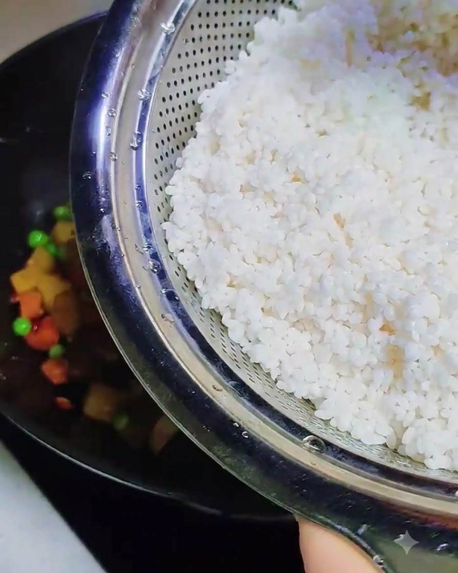 Riz gluant trempé et tendre versé dune passoire métallique dans le wok contenant les autres ingrédients cuits.
