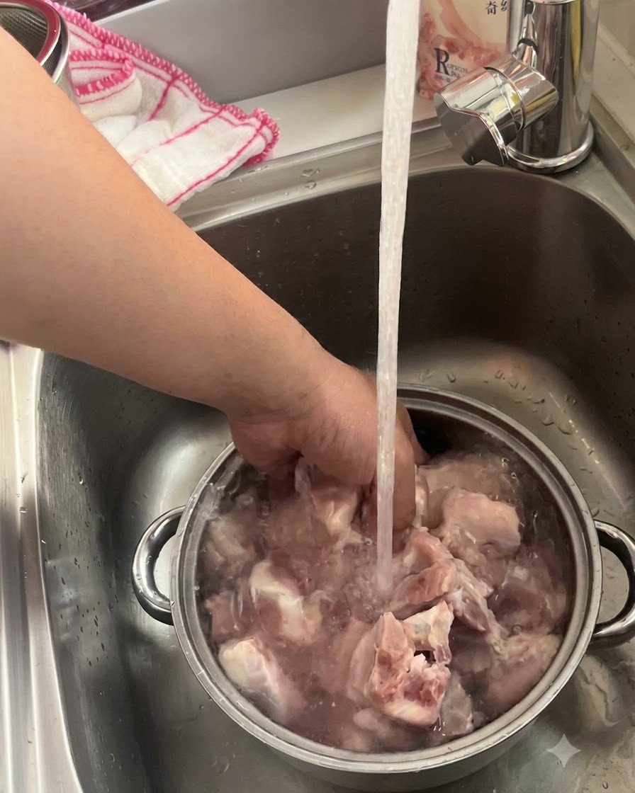 Côtes de porc fraîchement achetées en train de tremper et dêtre lavées dans un bol en métal sous un robinet de cuisine.