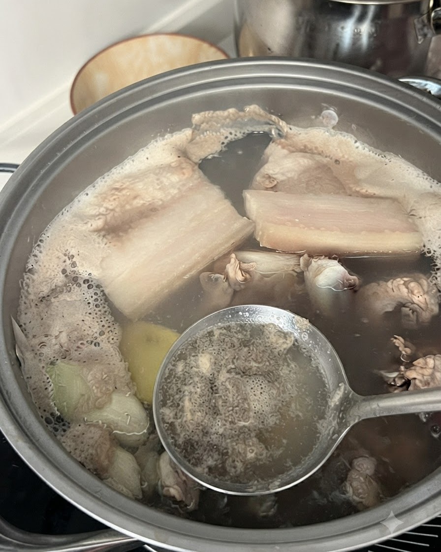 Une écumoire en train denlever la mousse grise et les impuretés de leau bouillante dans une casserole contenant des côtes de porc.