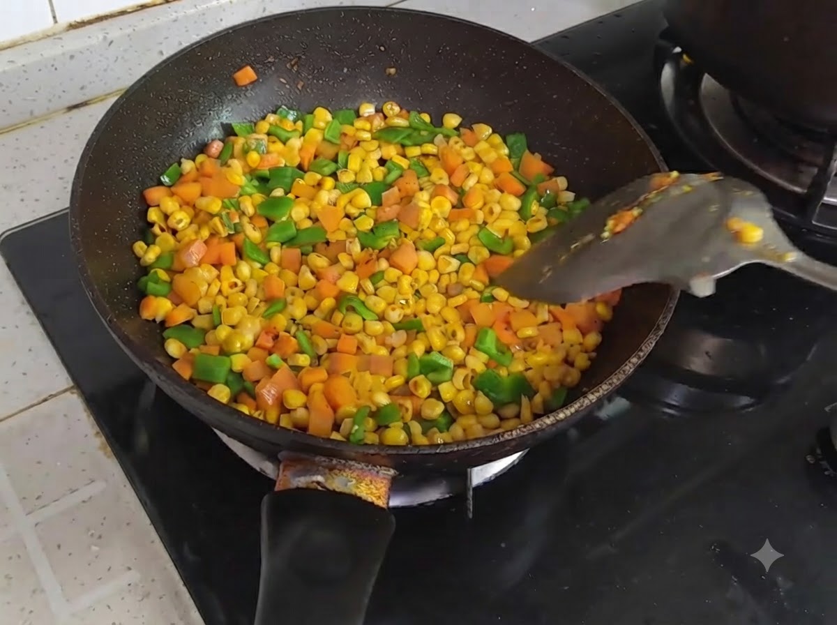 Poêle remplie de maïs, de carottes et de poivrons verts en dés en train dêtre mélangés avec une spatule.