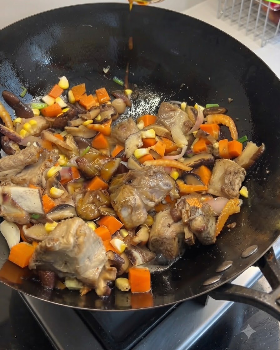 Des sauces soja noire et claire versées den haut dans un wok rempli de côtes de porc sautées, de carottes, de champignons et de maïs.