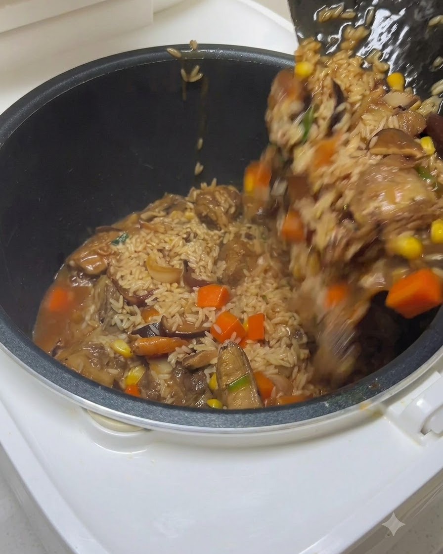 Une spatule transférant le riz assaisonné, les côtes et les légumes dans la cuve dun cuiseur de riz pendant que de leau est versée.
