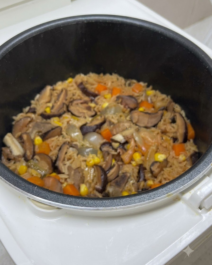 Du riz cuit mélangé avec des champignons, des carottes et du maïs à lintérieur de la cuve du cuiseur de riz juste avant lassaisonnement final.