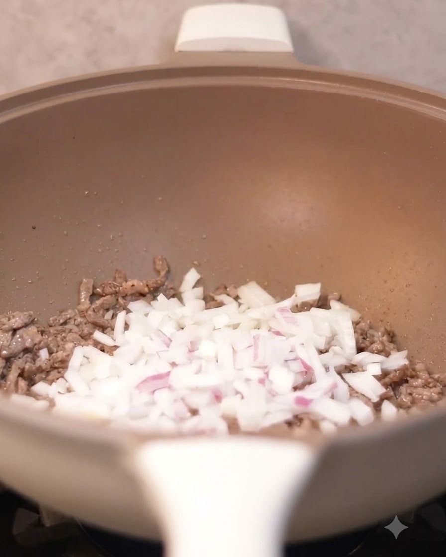 Oignons en dés versés dans le wok avec les morceaux de bœuf cuits.