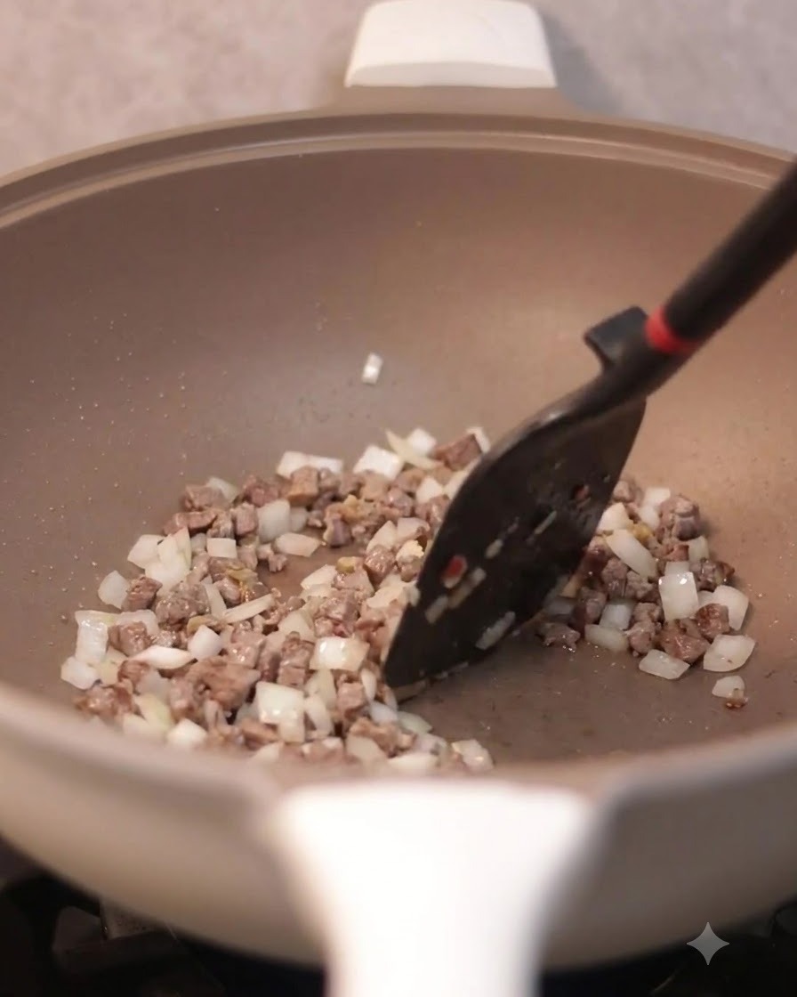 Une spatule remuant des œufs brouillés mélangés au bœuf et aux oignons dans une poêle.