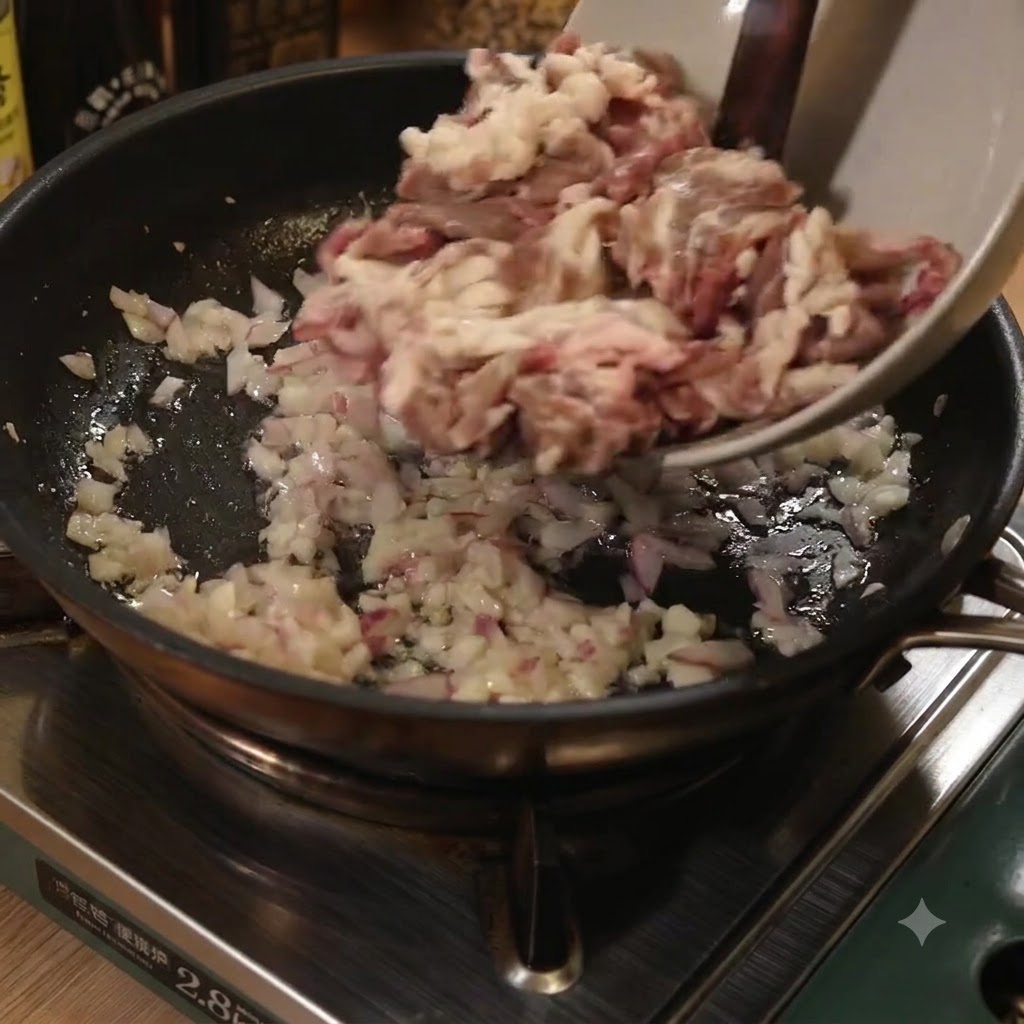 De fines lanières de bœuf ajoutées depuis un bol dans une poêle avec des oignons et de lail sautés.