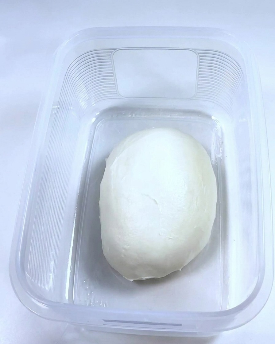 Une boule de pâte lisse reposant à lintérieur dun récipient en plastique rectangulaire propre et huilé.