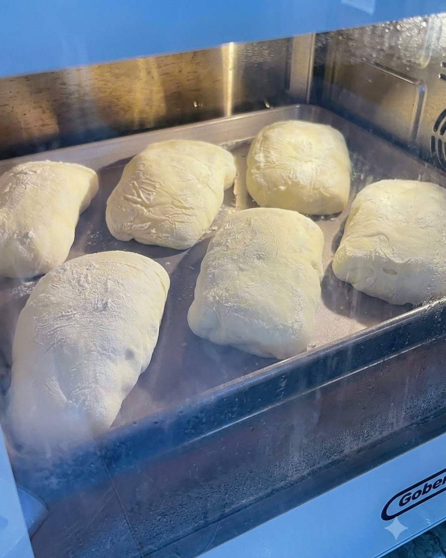 Pâte fermentée saupoudrée de farine posée sur une plaque de cuisson en métal à lintérieur dun four ou dune zone de pousse.