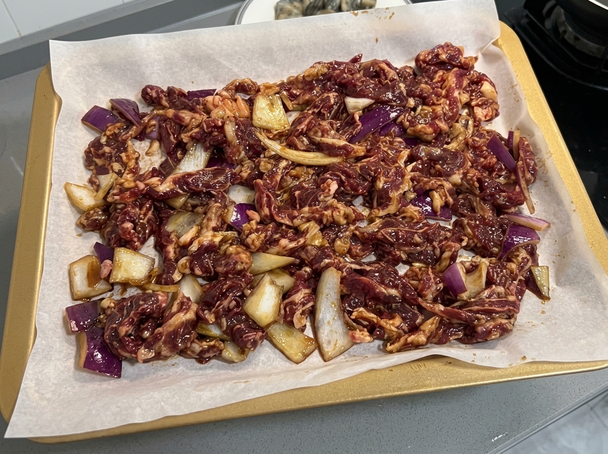 Bœuf mariné et tranches doignon disposés uniformément sur une plaque de cuisson recouverte de papier sulfurisé.