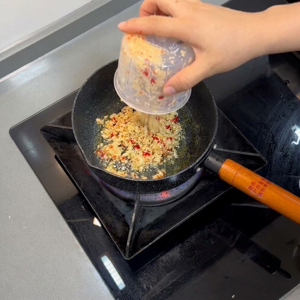 Ail haché et piments rouges en train de frire dans de lhuile chaude à lintérieur dune petite poêle.