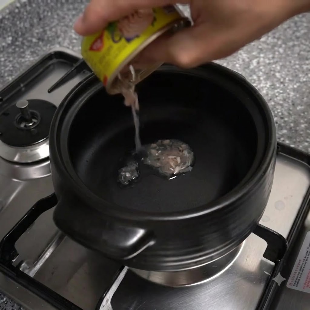 De lhuile sécoulant dune petite boîte de thon à étiquette jaune dans un pot en terre noir posé sur un brûleur de cuisinière.