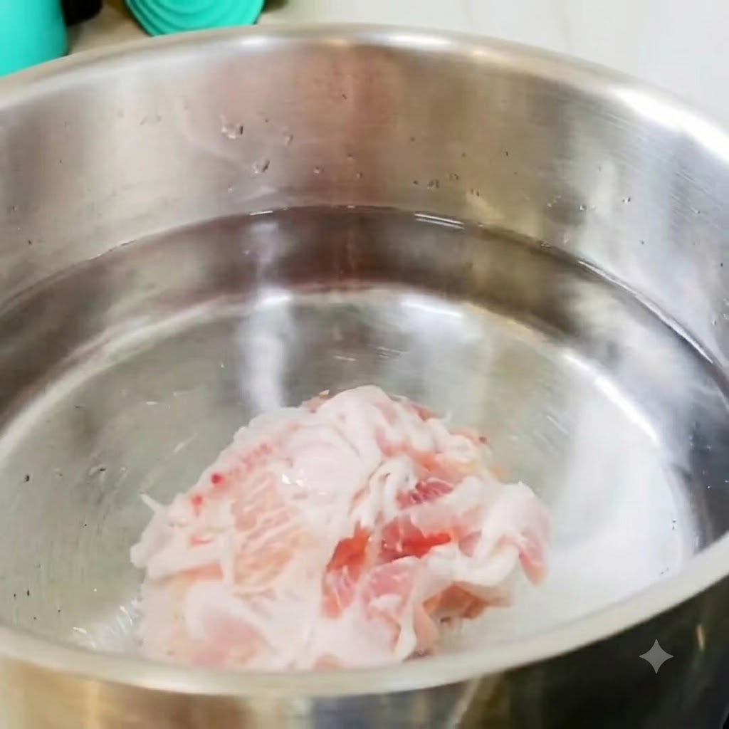 Des tranches de poitrine de porc et des morceaux de pommes de terre reposant dans une casserole en acier inoxydable remplie deau froide sur la cuisinière.