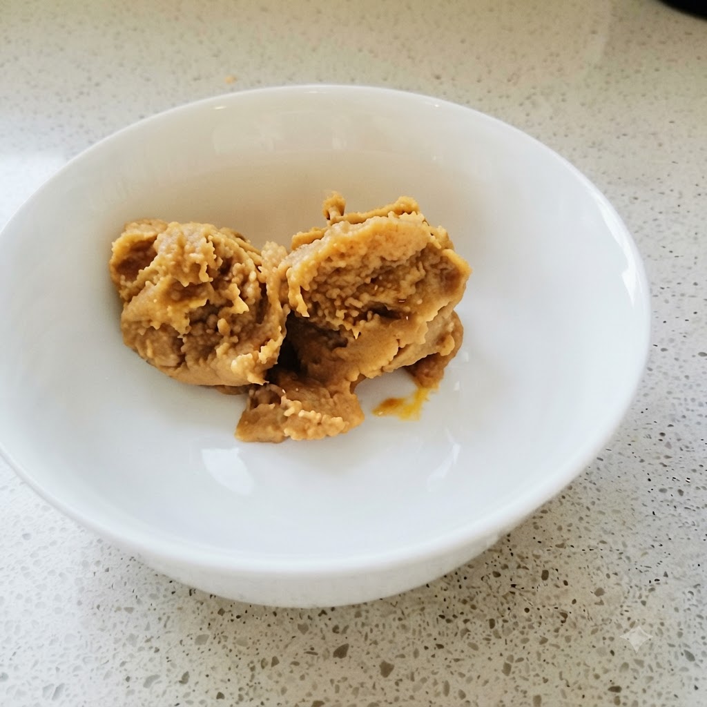 De la pâte de soja coréenne et de la pâte de piment mélangées soigneusement dans un bol blanc avec une cuillère dorée.