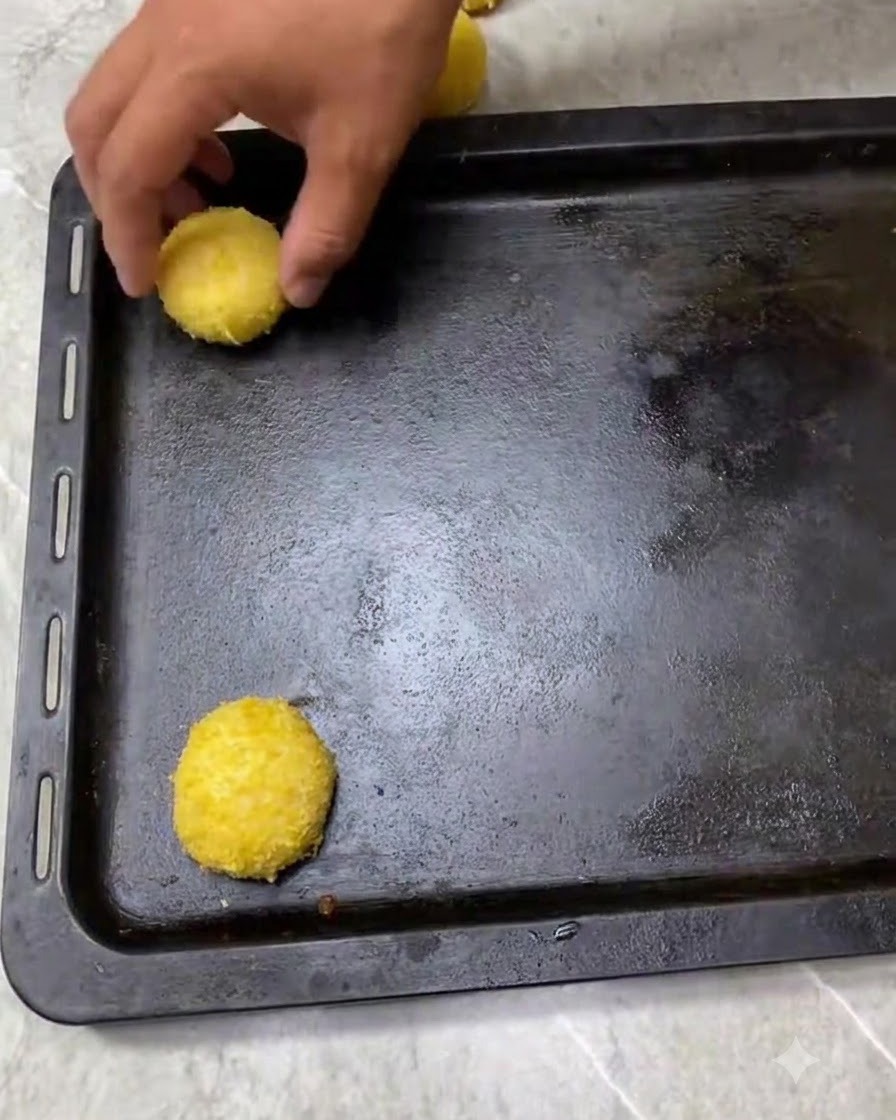Boules de pâte enrobées de chapelure espacées uniformément sur un plateau de cuisson sombre, prêtes pour lapprêt.