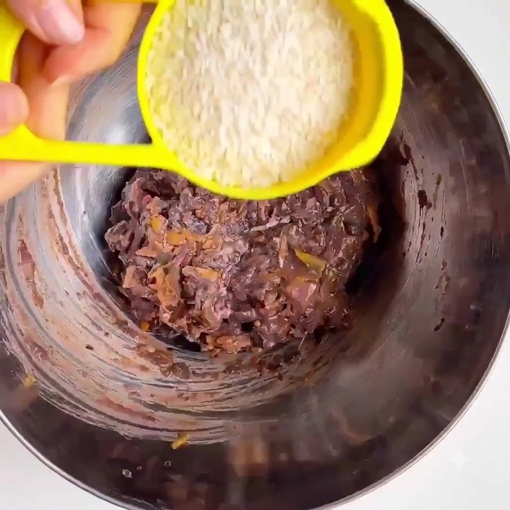 Farine davoine versée dune tasse à mesurer jaune dans un bol mélangeur en métal avec des haricots écrasés et des légumes.