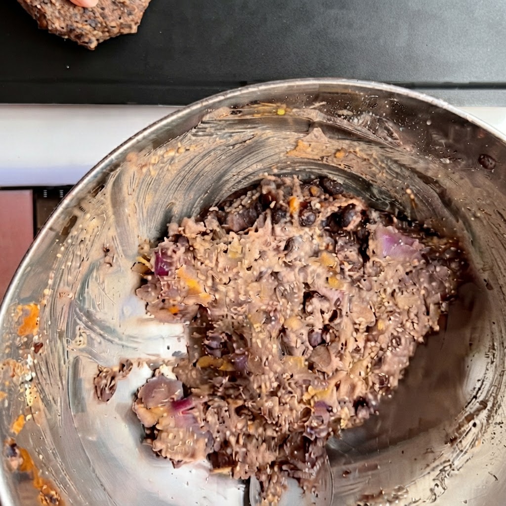 Plusieurs steaks de burger de haricots noirs façonnés disposés proprement sur une plaque de cuisson sombre.