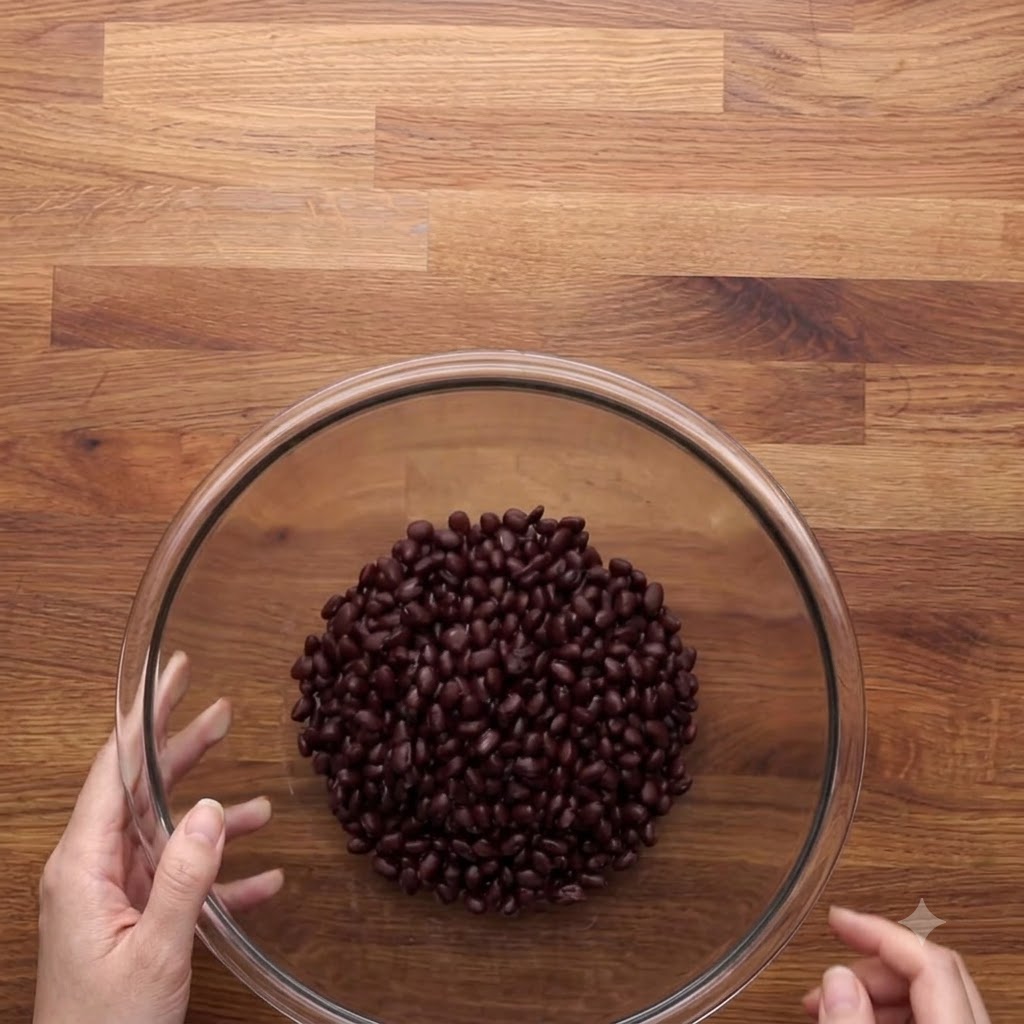 Haricots noirs rincés et égouttés dans un grand bol en verre transparent sur une surface en bois.