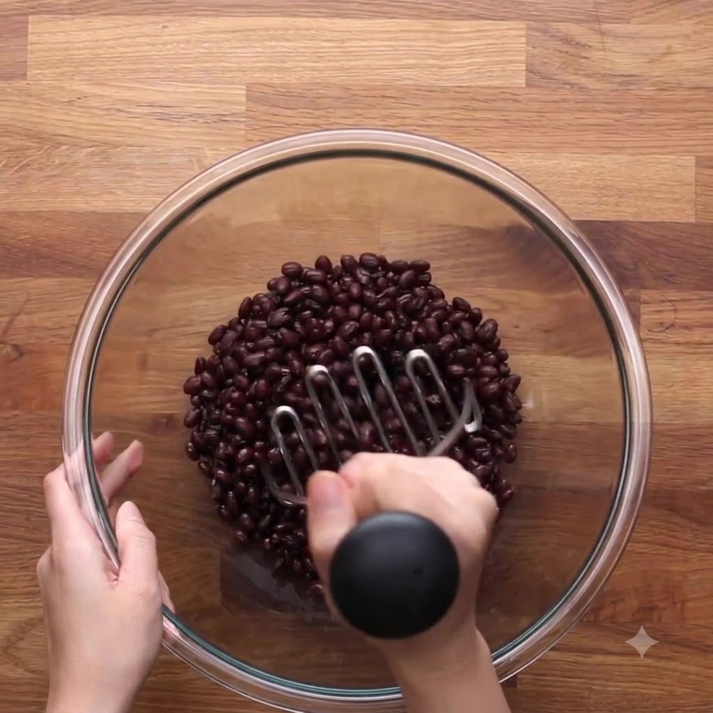 Un presse-purée en métal pressant des haricots noirs dans un bol.
