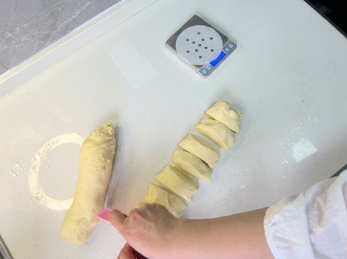 Des portions de pâte en cours de division et roulées à la main en petites boules rondes sur le plan de travail.