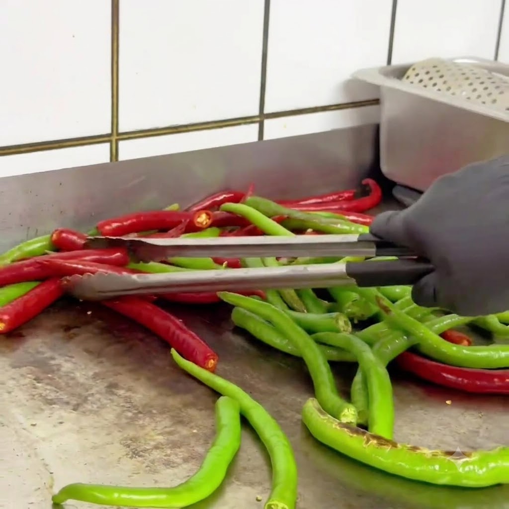Piments verts et rouges retournés avec des pinces dans une poêle chaude pendant quils roussissent.