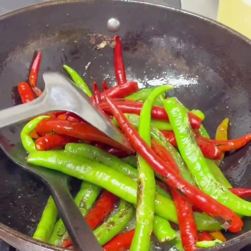 Piments boursouflés sautés avec une spatule dans un wok rempli dhuile épicée frémissante.