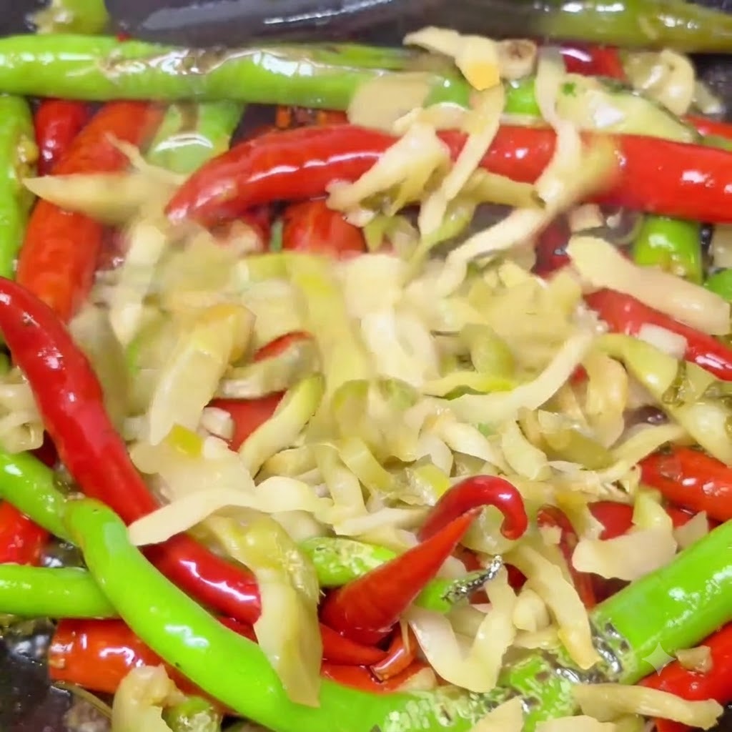 Feuilles de moutarde marinées mélangées à des piments rouges et verts boursouflés en train de sauter dans un wok chaud.