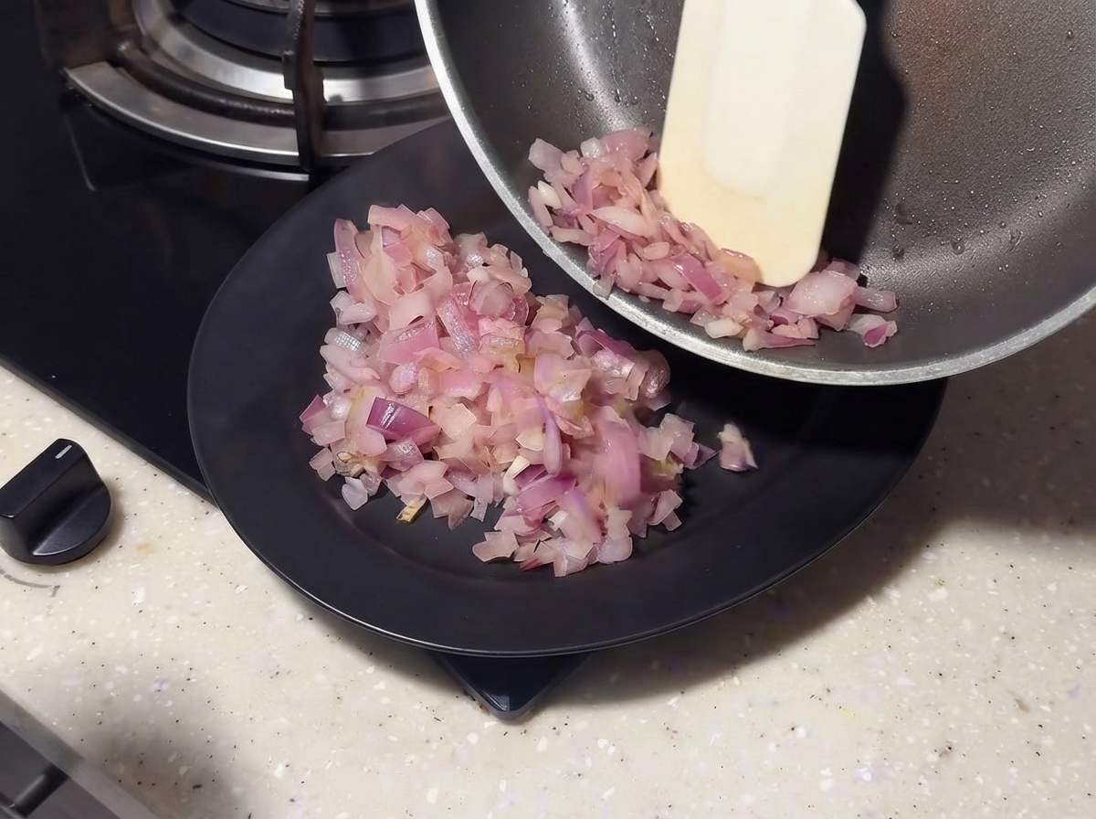 Des oignons sautés glissant dune poêle vers une assiette noire à laide dune spatule.