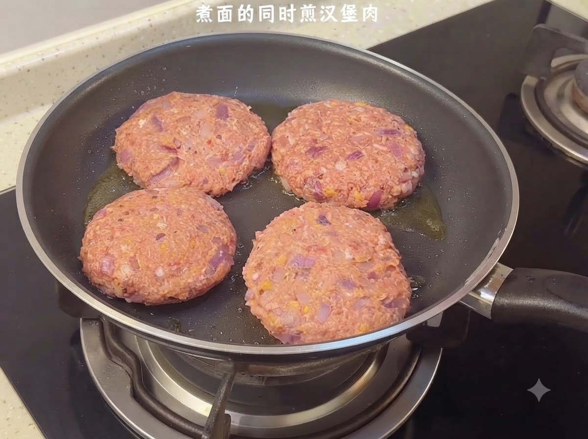 Quatre steaks hachés crus grésillant dans une poêle sur la cuisinière.