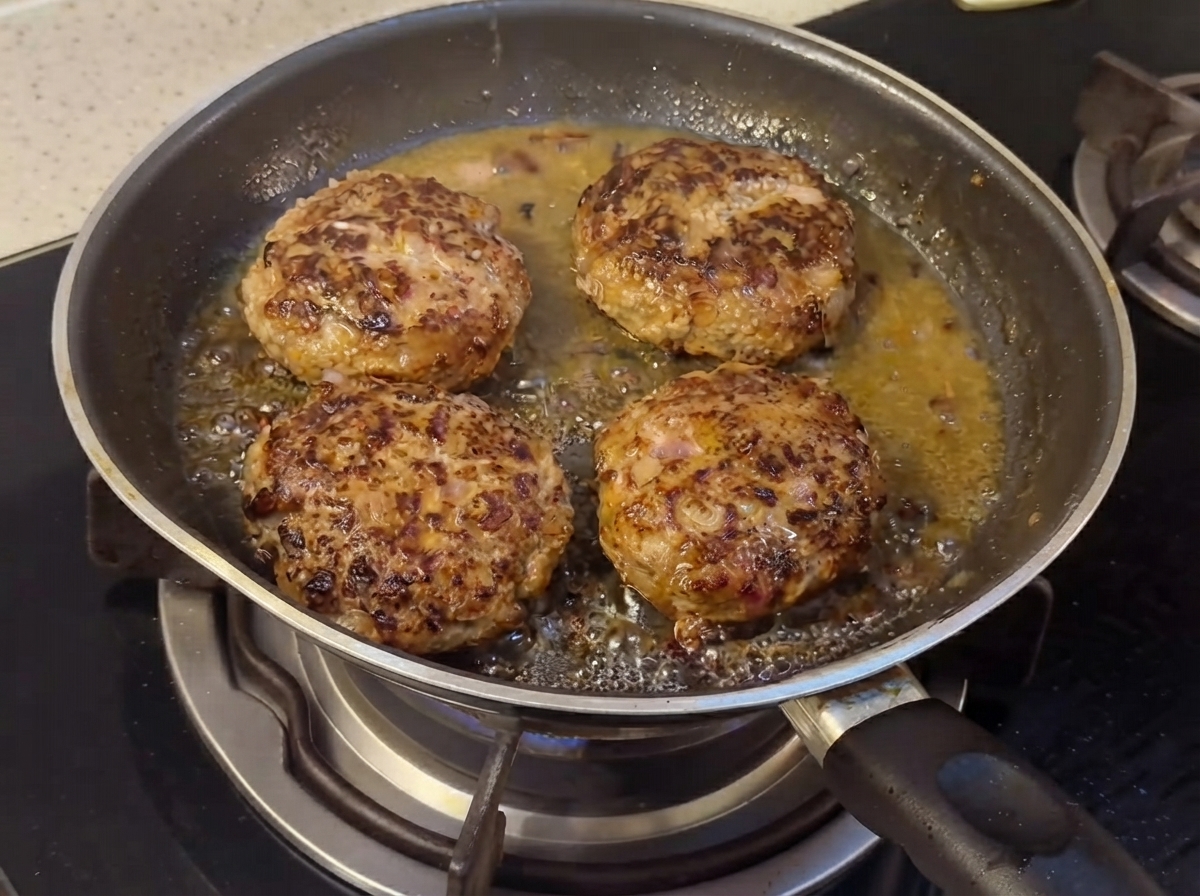 Des steaks hachés cuisant dans une poêle avec des ingrédients de sauce liquide qui commencent à se mélanger.