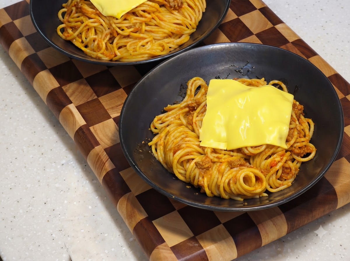 Une tranche de fromage jaune fondant sur la base de spaghettis à lintérieur dun bol de service noir.