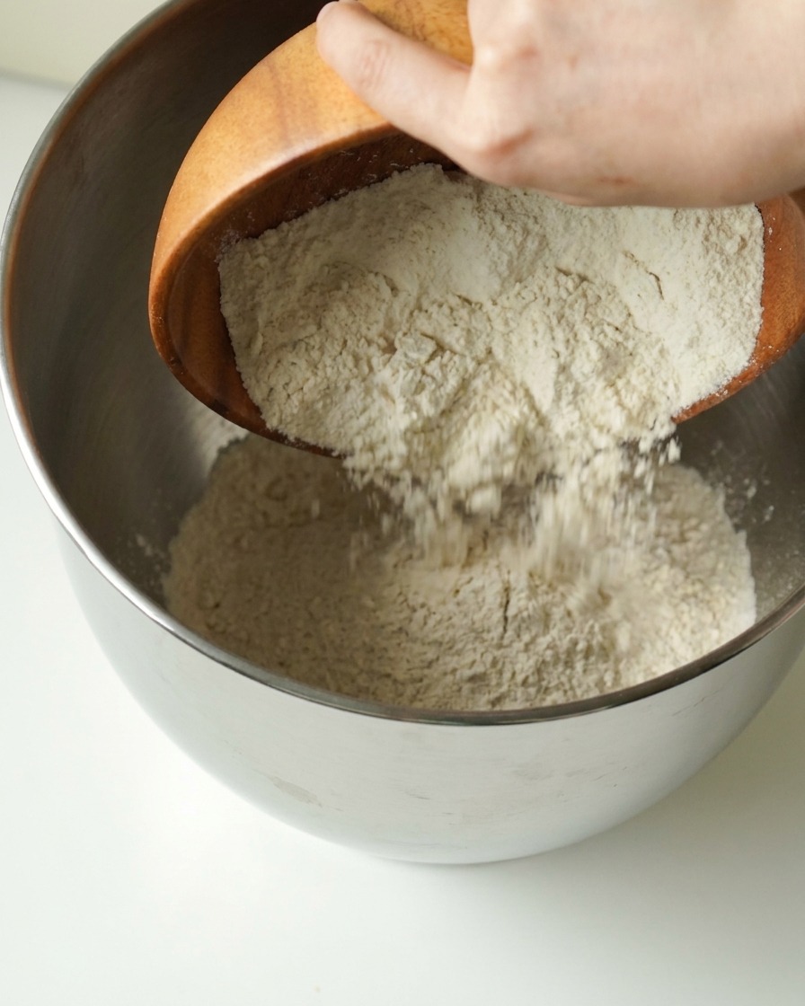 Farine versée dun bol en bois dans un grand bol mélangeur en métal.